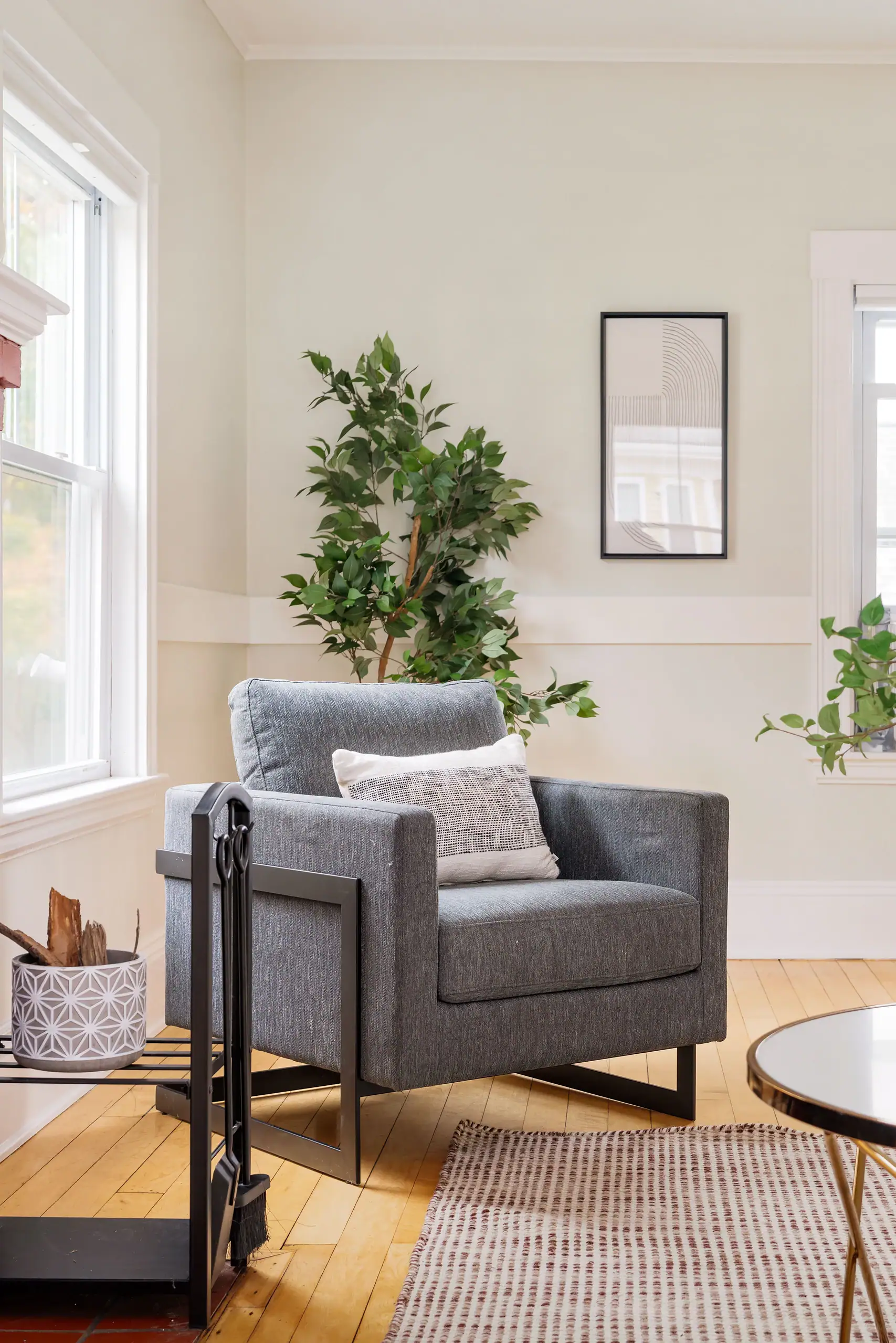 Modern living room with gray chair, potted plants, hardwood floors, and natural light in Boston property
